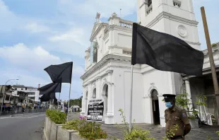 A policeman stands guard at St. Anthony's church in Colombo, Aug. 21, 2021, next to a placard and black flags placed in protest for the alleged failure to prosecute those responsible for the bomb attacks of Easter Sunday 2019. Credit: Ishara S. Kodikara/AFP via Getty Images. null